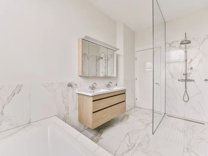Baño con porcelánico imitación mármol, mueble suspendido de madera con armario de espejo y mampara fija de vidrio, reformas de baño Zaragoza
