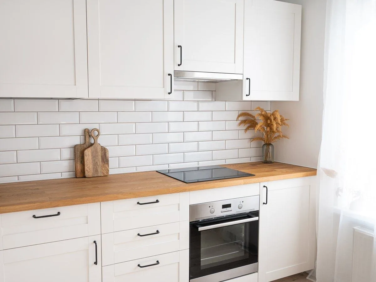 Cocina lineal blanca con encimera de madera, placa de inducción y horno, reformas low cost Zaragoza