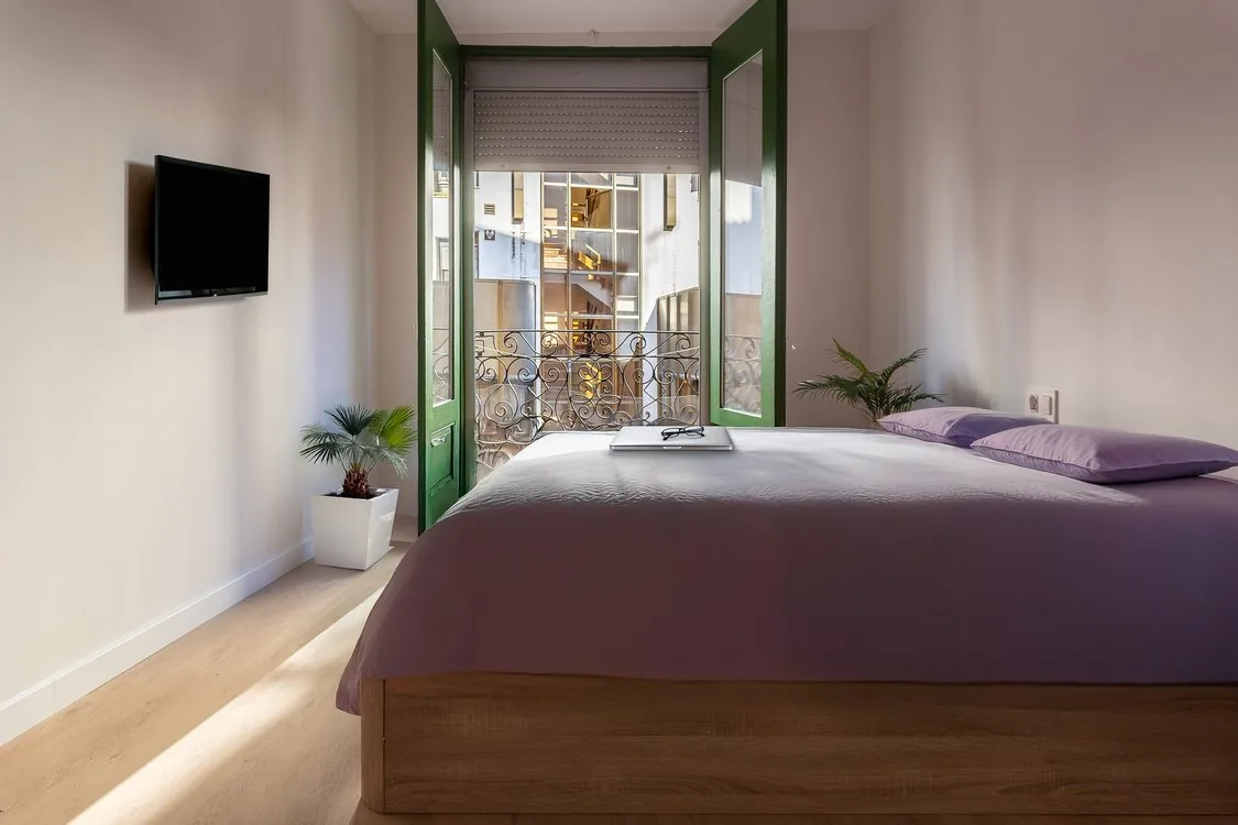 Dormitorio reformado con suelo de madera clara y balcón con barandilla de forja, renovación de suelo antiguo en Zaragoza