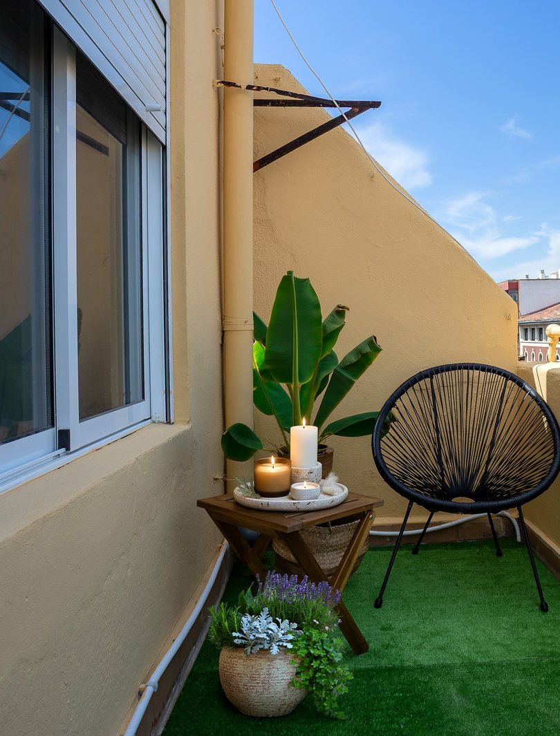 Terraza reformada con césped artificial, plantas y sillón de cuerda