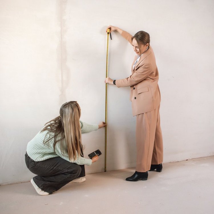 Dos personas tomando las medidas de una pared con cinta métrica antes de la reforma