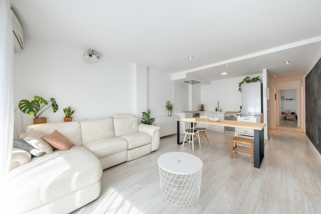Zona de estar diáfana con sofá, mesa de comedor y cocina abierta al fondo